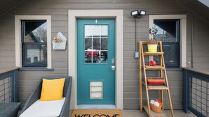 A front door with a 'WELCOME' mat, a wicker chair with a yellow cushion, and a wooden ladder with potted plants. - The Loft on Humphreys:  A Charming 2 BR Apartment in Downtown Flagstaff with A/C (Flagstaff)
