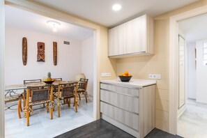 A modern kitchen with light wood cabinets, a dining area with a table and chairs, and decorative wall art. - Aquamijas Retreat – Modern Comfort Near Aguamijas Water Park (Mijas Costa)