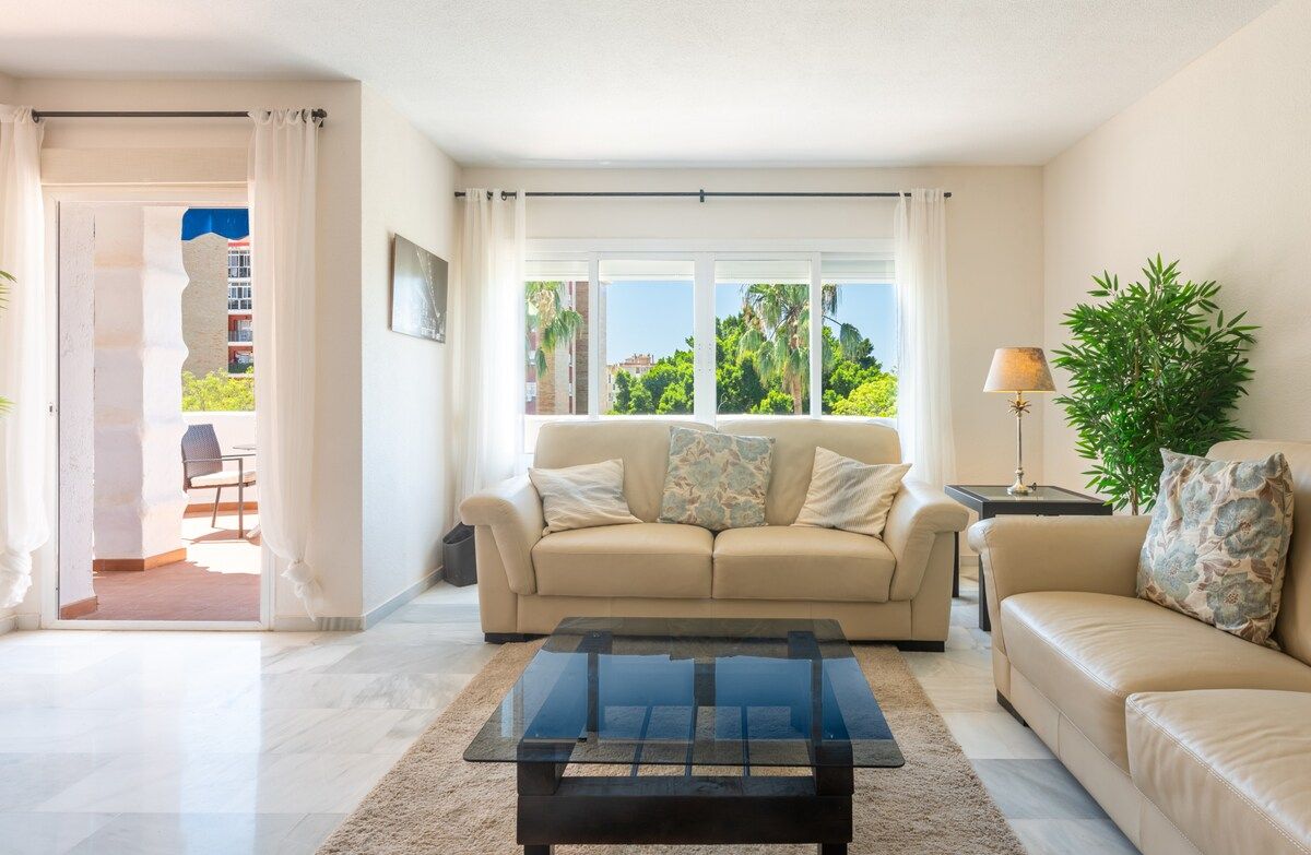 A living room with a sofa, a coffee table, and a view of greenery outside.