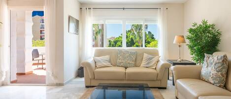 A living room with a sofa, a coffee table, and a view of greenery outside.