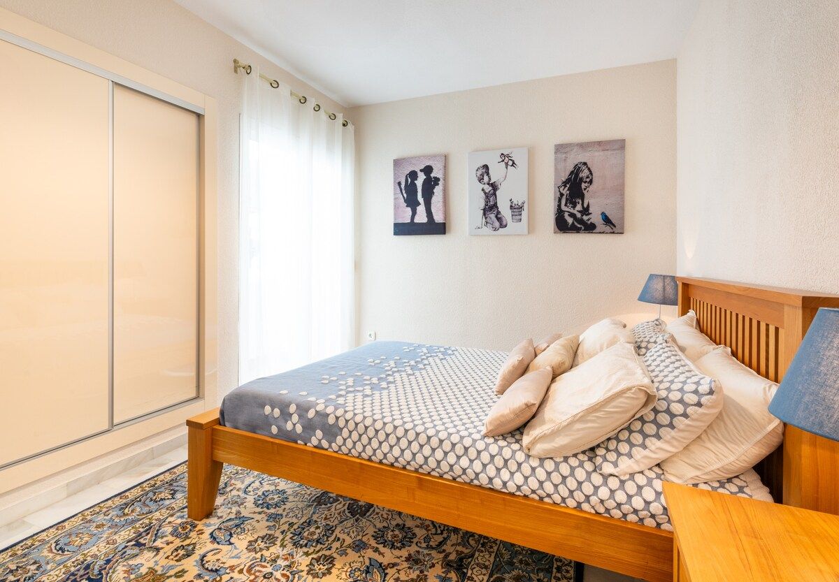 A bedroom with a bed, a nightstand, a lamp, and artwork on the wall.