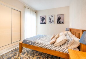 Une chambre à coucher avec un lit, une table de chevet, une lampe et des œuvres d’art accrochées au mur.