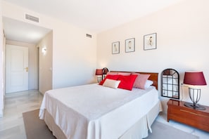A bedroom with a bed, bedside tables, and a nightstand. There are wall-mounted lamps and framed pictures on the wall. - Aquamijas Retreat – Modern Comfort Near Aguamijas Water Park (Mijas Costa)