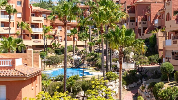 Een resort met meerdere gebouwen, een zwembad, palmbomen en een rotsachtig landschap.