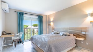 Een slaapkamer met een bed, een bureau en een stoel. Er is een balkon met uitzicht op groen.