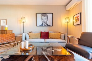 Een moderne woonkamer met een glazen salontafel, een bank, een leren fauteuil en twee vloerlampen.