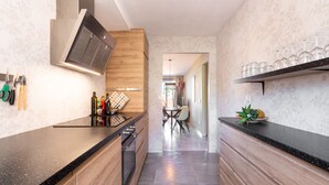 Een moderne keuken met houten kastjes, een zwart aanrecht en een ingebouwde kookplaat. Achtergrond toont een eethoek met een tafel en stoelen.