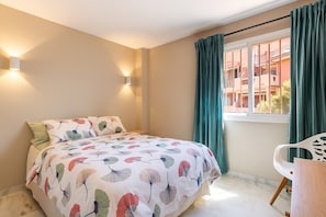 A bedroom with a bed, a window with curtains, a chair, and wall-mounted lights.