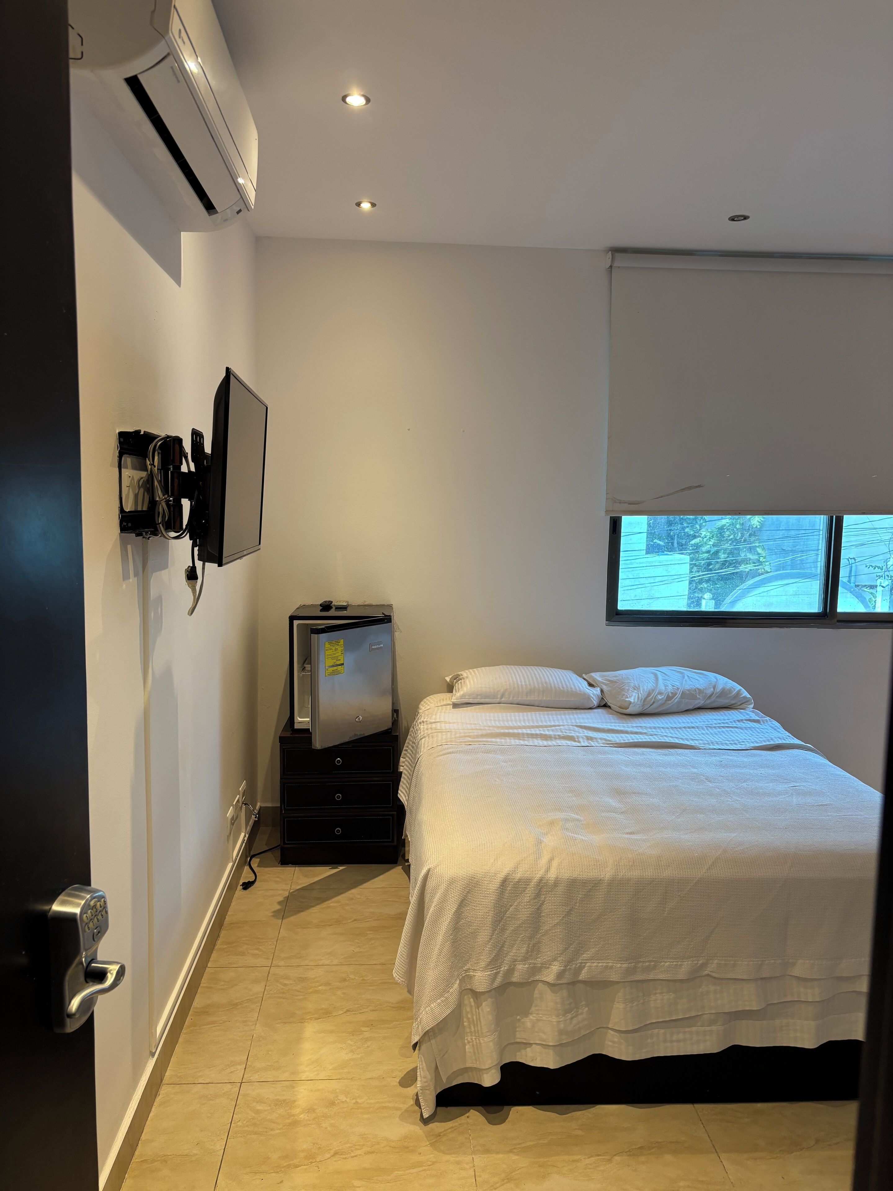 A bedroom with a bed, a TV, an air conditioner, and a window.