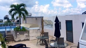 A rooftop terrace with lounge chairs, a glass table, and a pool in the background. - 770 Apartments (Playa del Carmen)