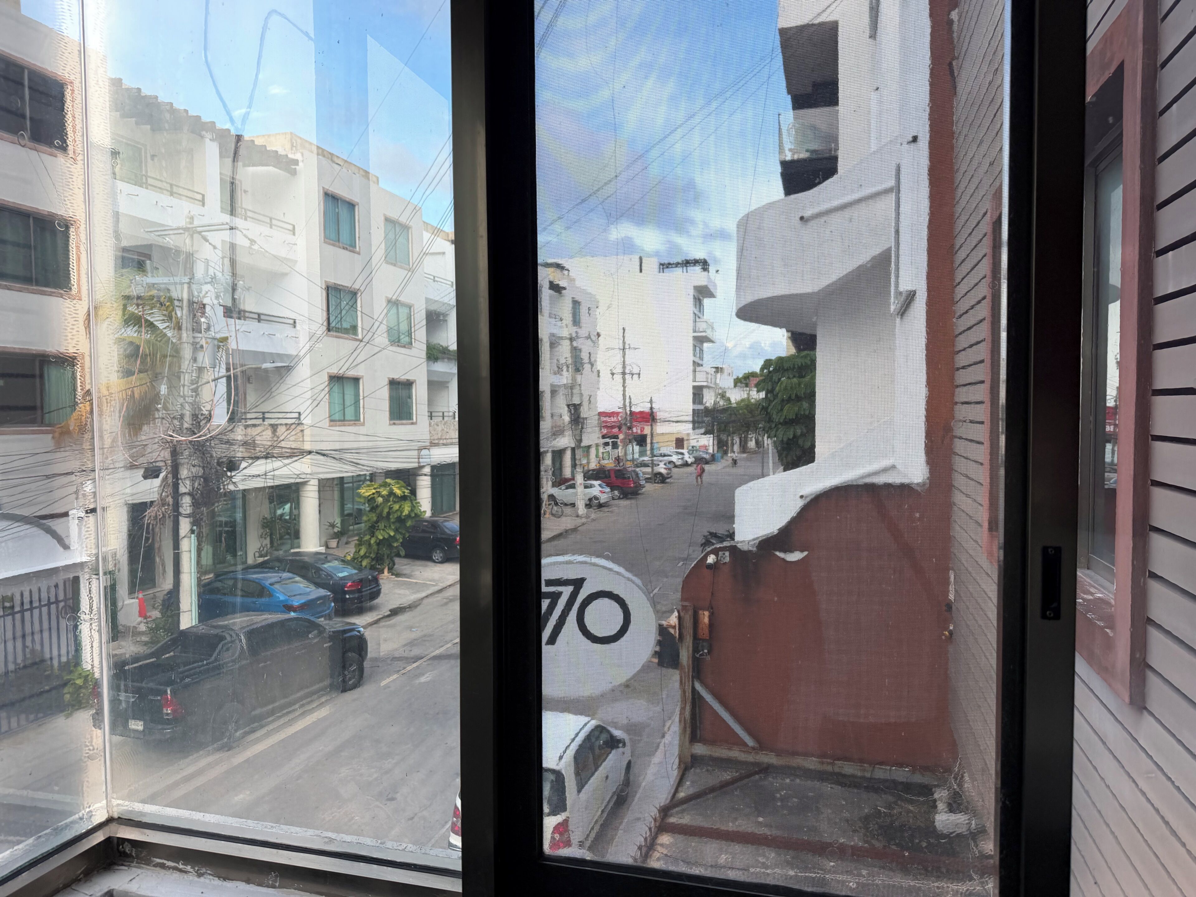 Vista a través de una ventana que muestra una calle con edificios, coches estacionados y una señal de límite de velocidad.