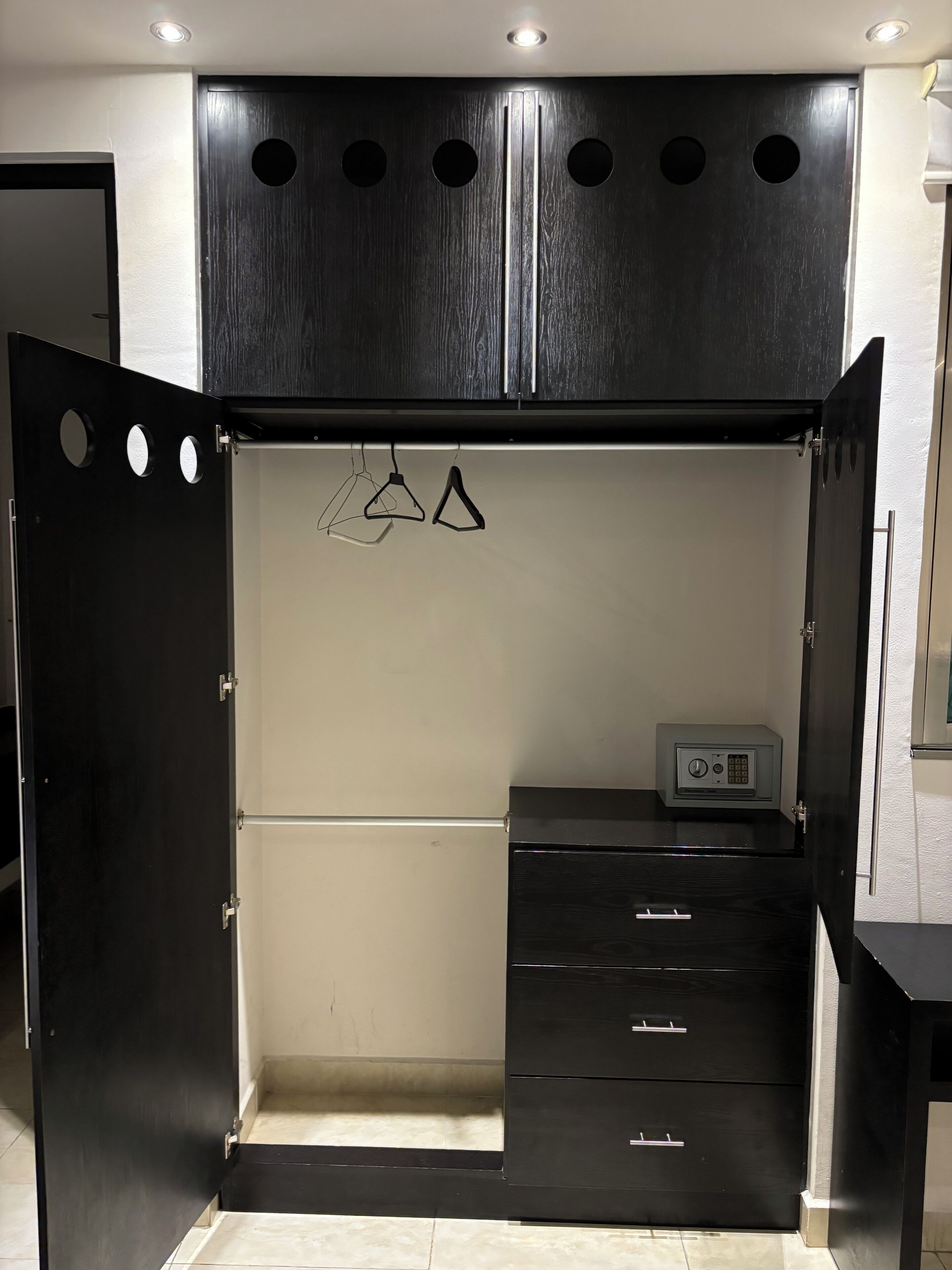 Une pièce comprenant une armoire avec une combinaison de portes ouvertes et fermées, un petit bureau doté de tiroirs et un dispositif de sécurité placé sur le bureau.