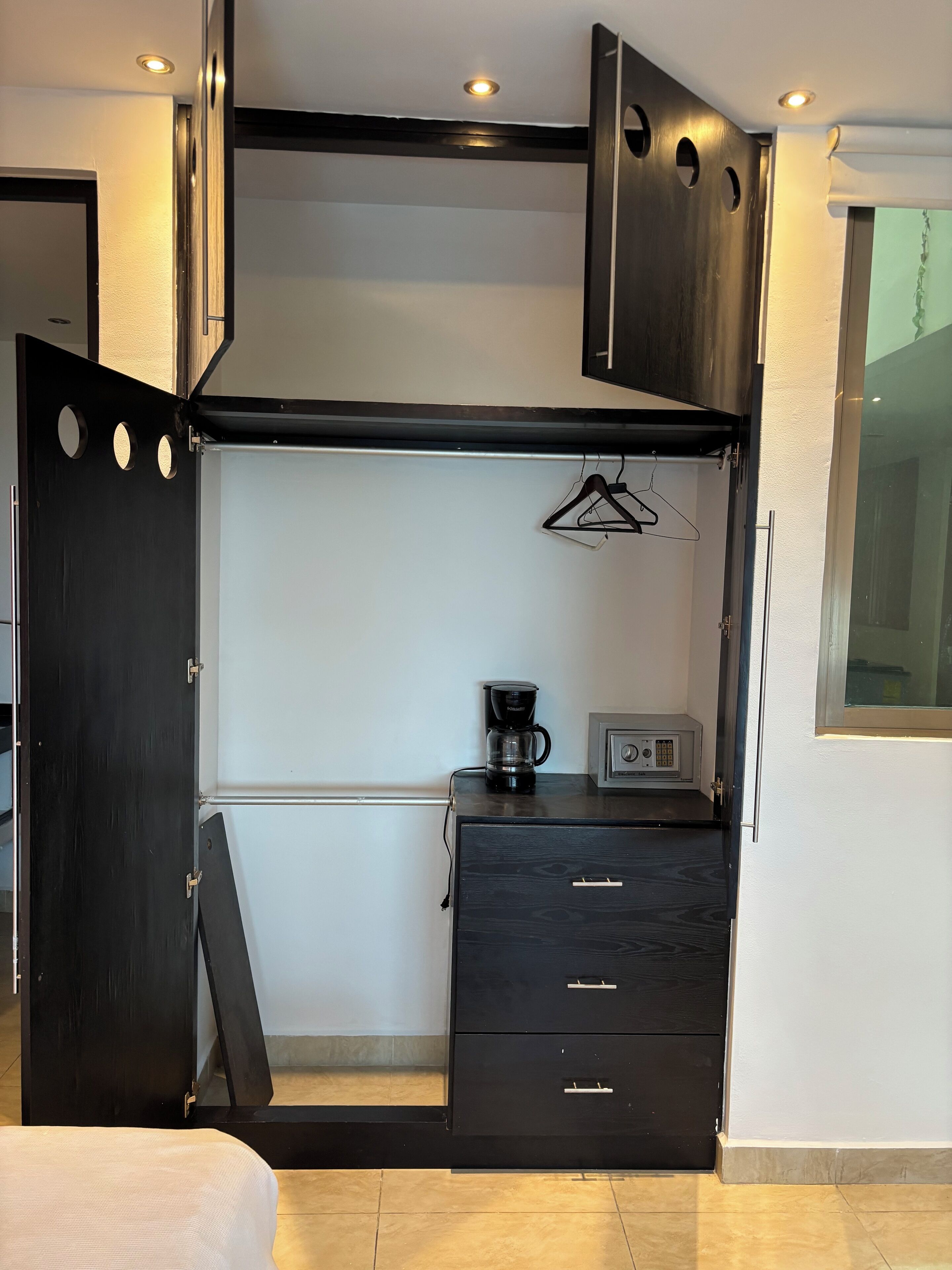 Een compacte kamer met een bed, een kleine kitchenette met een koffiezetapparaat, en een garderobe met meerdere lades.