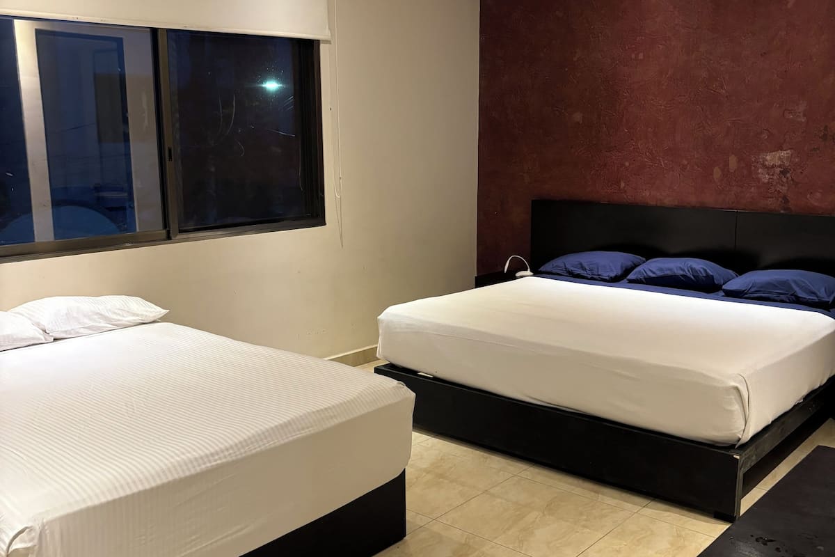 Un dormitorio moderno con dos camas, un ventanal grande y una pared de acento roja.