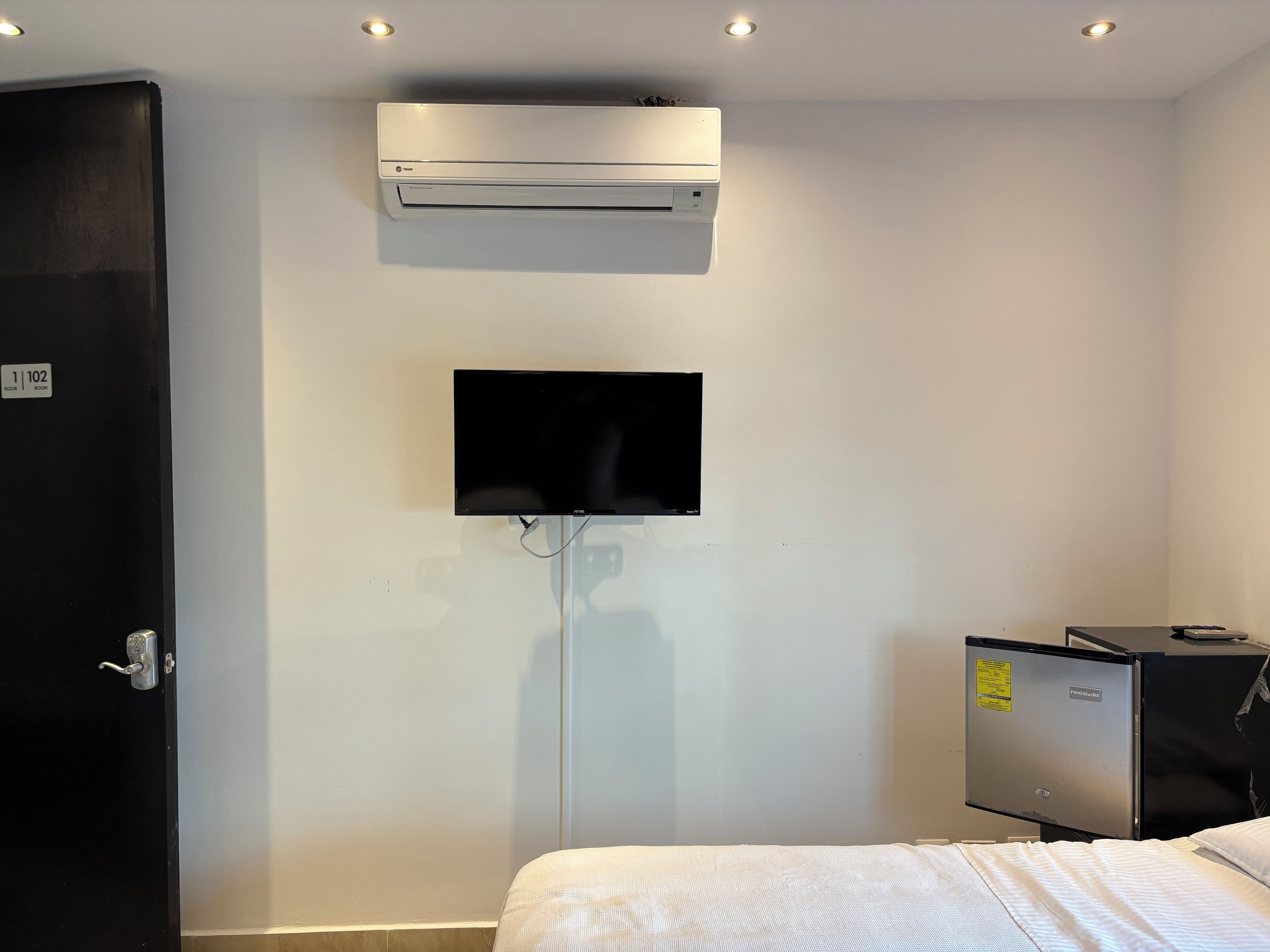 Een hotelkamer met een bed, een aan de muur bevestigde televisie en een airconditioningunit erboven.