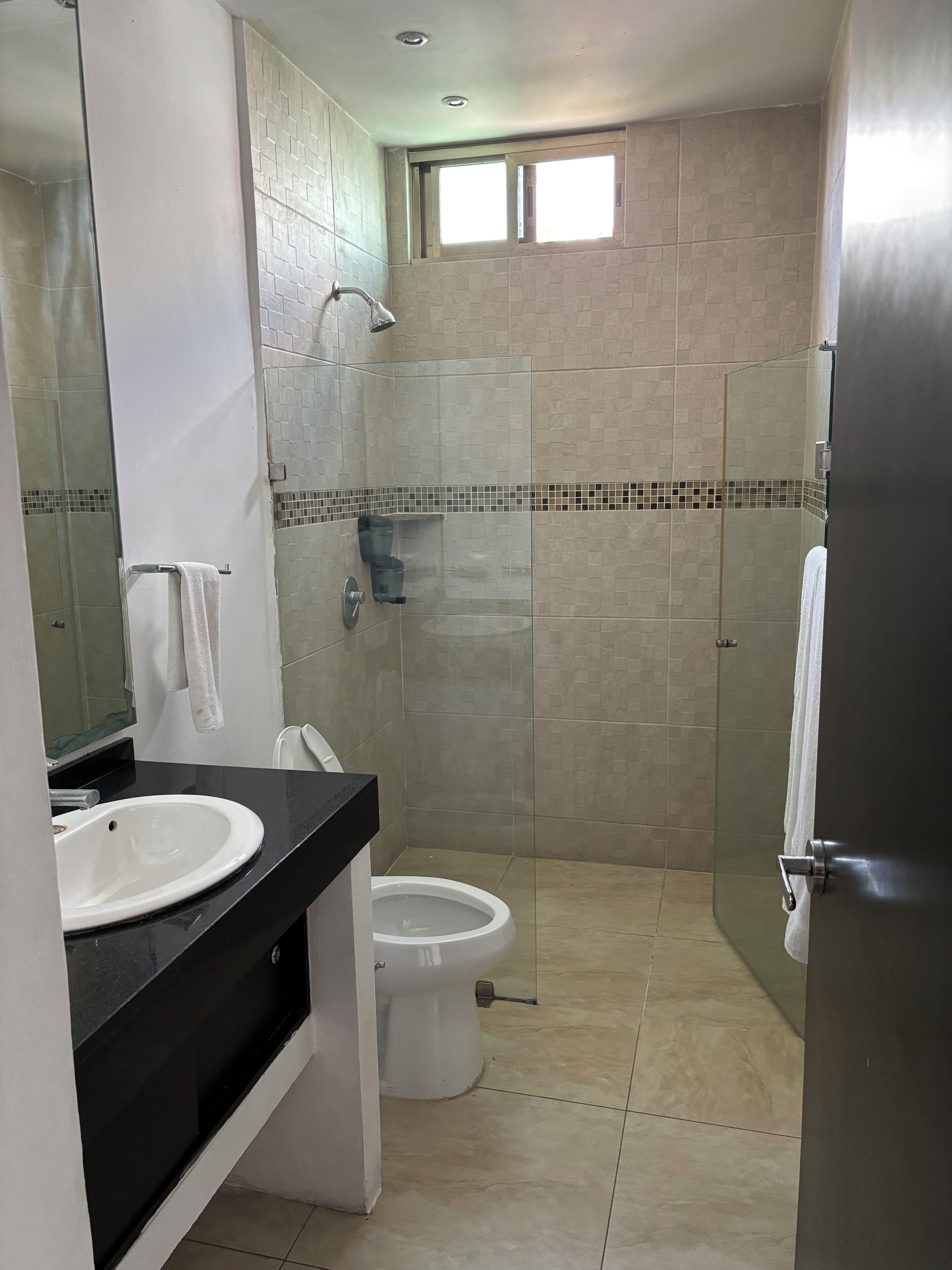 Un baño con lavamanos blanco, inodoro y zona de ducha con mampara de vidrio.