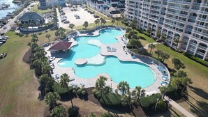 A resort with a large central pool, multiple smaller pools, and a variety of sun loungers and umbrellas. - Barefoot Havens 325 - Golf, Shopping, Dining, Pool (North Myrtle Beach)