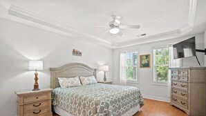 A bedroom with a bed, nightstands, a dresser, a ceiling fan, and a window with blinds. - Barefoot Havens 325 - Golf, Shopping, Dining, Pool (North Myrtle Beach)