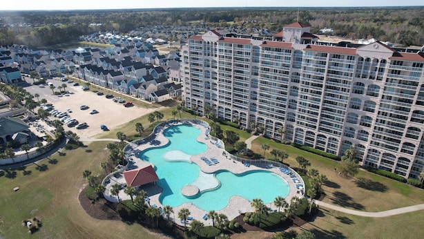 A large hotel with multiple buildings, a central swimming pool, and surrounding greenery. - Barefoot Havens 325 - Golf, Shopping, Dining, Pool (North Myrtle Beach)