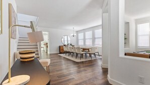 Un salon moderne avec un parquet en bois foncé, une table ronde entourée de chaises, une lampe et un grand miroir.