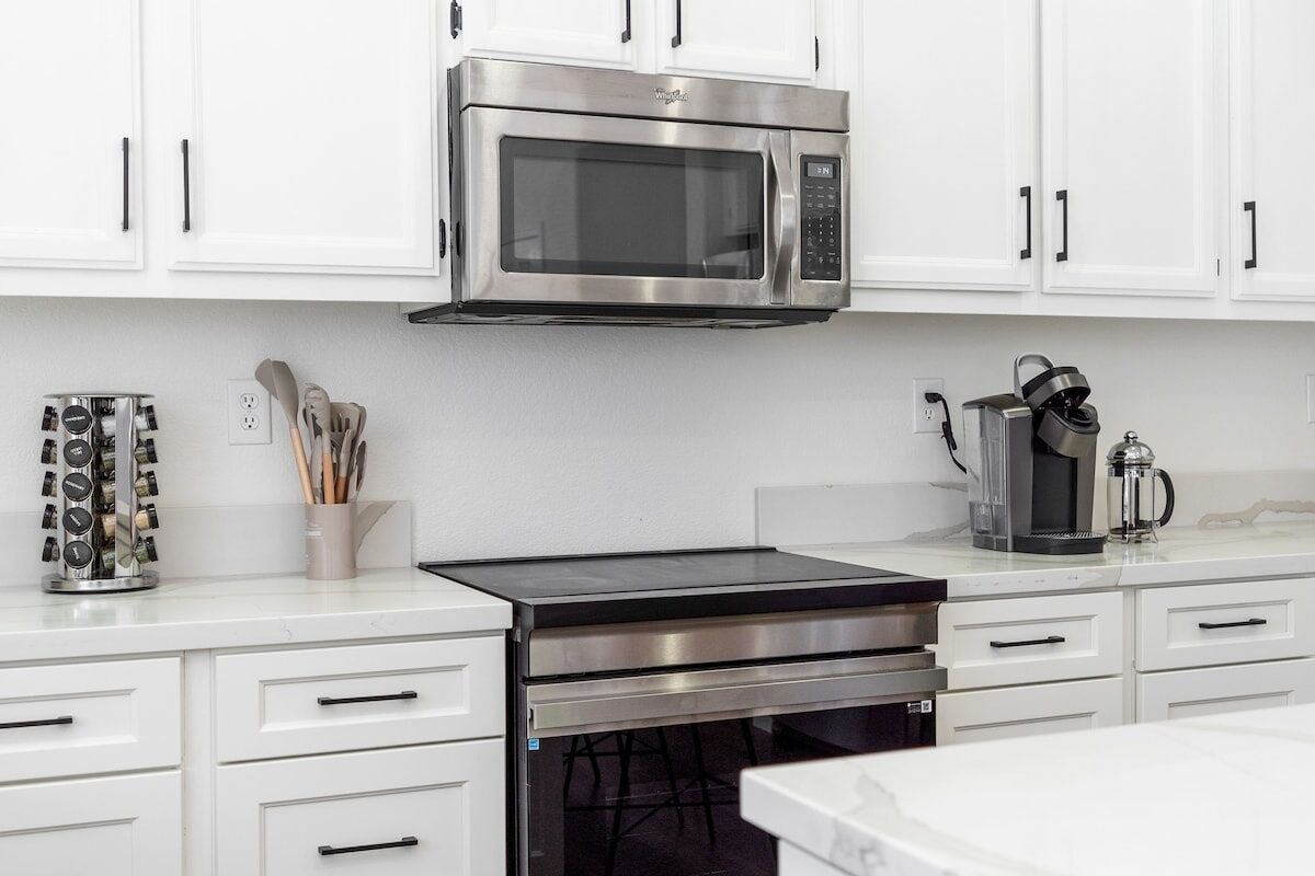 A modern kitchen with white cabinets, a stainless steel microwave, a coffee maker, and a kettle on the countertop.