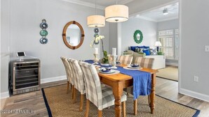 A dining area with a wooden table, chairs, and a chandelier. There is a mirror on the wall and a small cabinet with a device on top. - Sawgrass Country Club - 26 Tifton Way - Stunning Golf Course Views! (Ponte Vedra Beach)