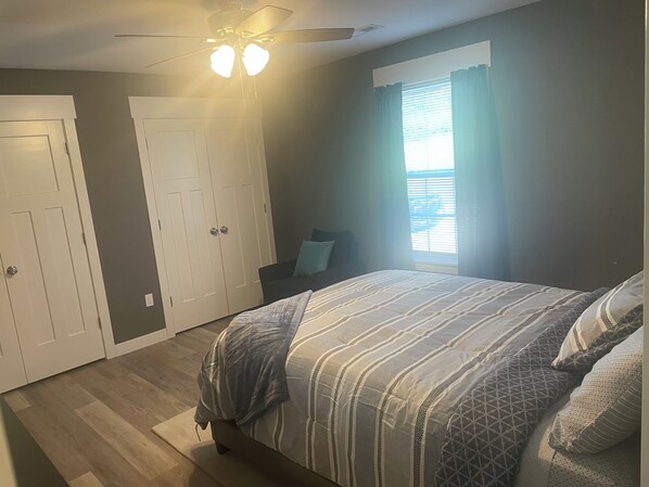 Un dormitorio con cama, ventilador de techo, ventana con cortinas y armario.