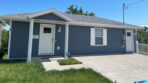 A single-story house with a white door and window shutters, a small porch, and a number '915' on the door.