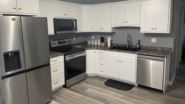 A modern kitchen with white cabinets, stainless steel appliances, a microwave, stove, oven, and a sink.