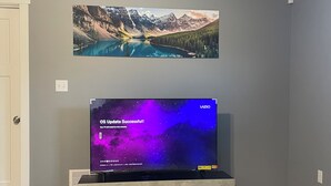 A flat-screen TV on a stand with a cosmic-themed wallpaper, mounted on a wall above a wooden floor.