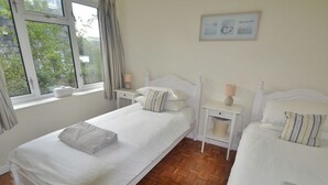 Un dormitorio con dos camas, una ventana con cortinas, una mesita de noche con lámpara y un cuadro en la pared.
