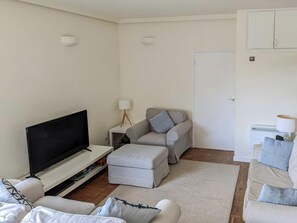 Un salon comprenant un téléviseur à écran plat, un canapé, un pouf, une table basse et une lampe.