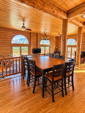 A log cabin interior with a large dining table, chairs, a television, and a ceiling fan.