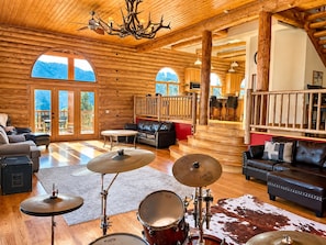 A log cabin interior with a drum set, leather furniture, and a view of the outdoors.