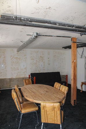 Una habitación con una mesa redonda de madera rodeada de sillas de cuero, un sofá negro y un pilar de madera.
