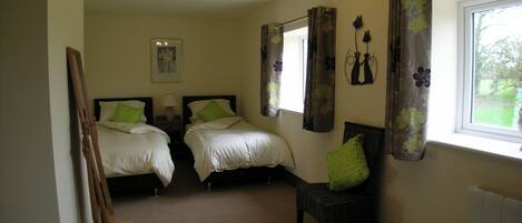 A bedroom with two beds, a chair, a radiator, a window with curtains, and a chandelier.