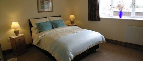 A bedroom with a bed, two bedside lamps, a nightstand, a window with curtains, and a wall-mounted picture.