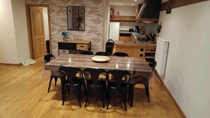 Een eetruimte met een houten tafel en stoelen, een keuken op de achtergrond en een bakstenen muur.