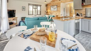 Une cuisine moderne avec un plafond en bois, un coin repas avec une table dressée pour deux personnes, et un salon avec un canapé bleu.