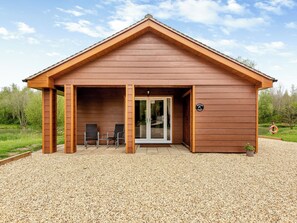 A wooden cabin with a covered patio area, two chairs, and a door leading to the interior.