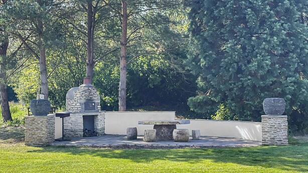 Un espacio al aire libre construido en piedra, con un horno de piedra, asientos y una mesa pequeña.