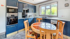 Una cocina moderna con armarios azules, horno empotrado, microondas y un comedor con mesa redonda y sillas de madera.