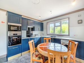 A modern kitchen with blue cabinets, a built-in oven, a microwave, and a dining area with a round table and wooden chairs.