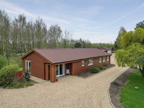 A single-story wooden building with a sloped roof, a gravel driveway, and a surrounding garden.
