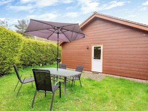 A patio with a table and chairs, a purple umbrella, and a wooden building with a door.