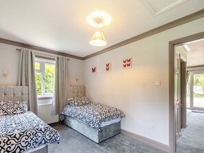 A bedroom with two beds, a window with curtains, a wall-mounted light fixture, and a door leading outside.