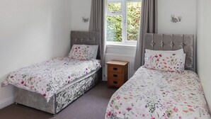 Un dormitorio con dos camas, una ventana con cortinas, un radiador y una mesita de noche de madera.