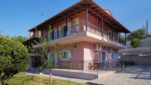 Un edificio de dos pisos con balcones, un muro de piedra y cielo despejado.
