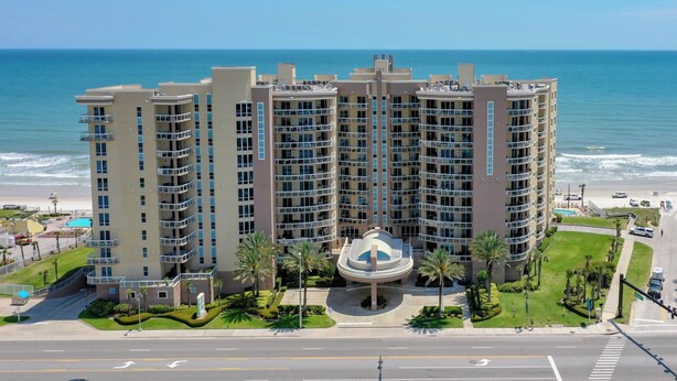 A multi-story hotel with a central courtyard, located near a beach with ocean views.