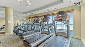 A gym with treadmills, exercise bikes, and a ceiling fan.